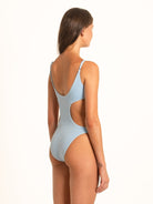 Slight back angle of model in textured blue monokini with waist cutout and soft straps