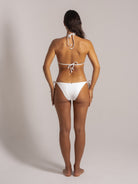 Back full view of woman wearing white triangle bikini with halter neck and tie-side bottoms