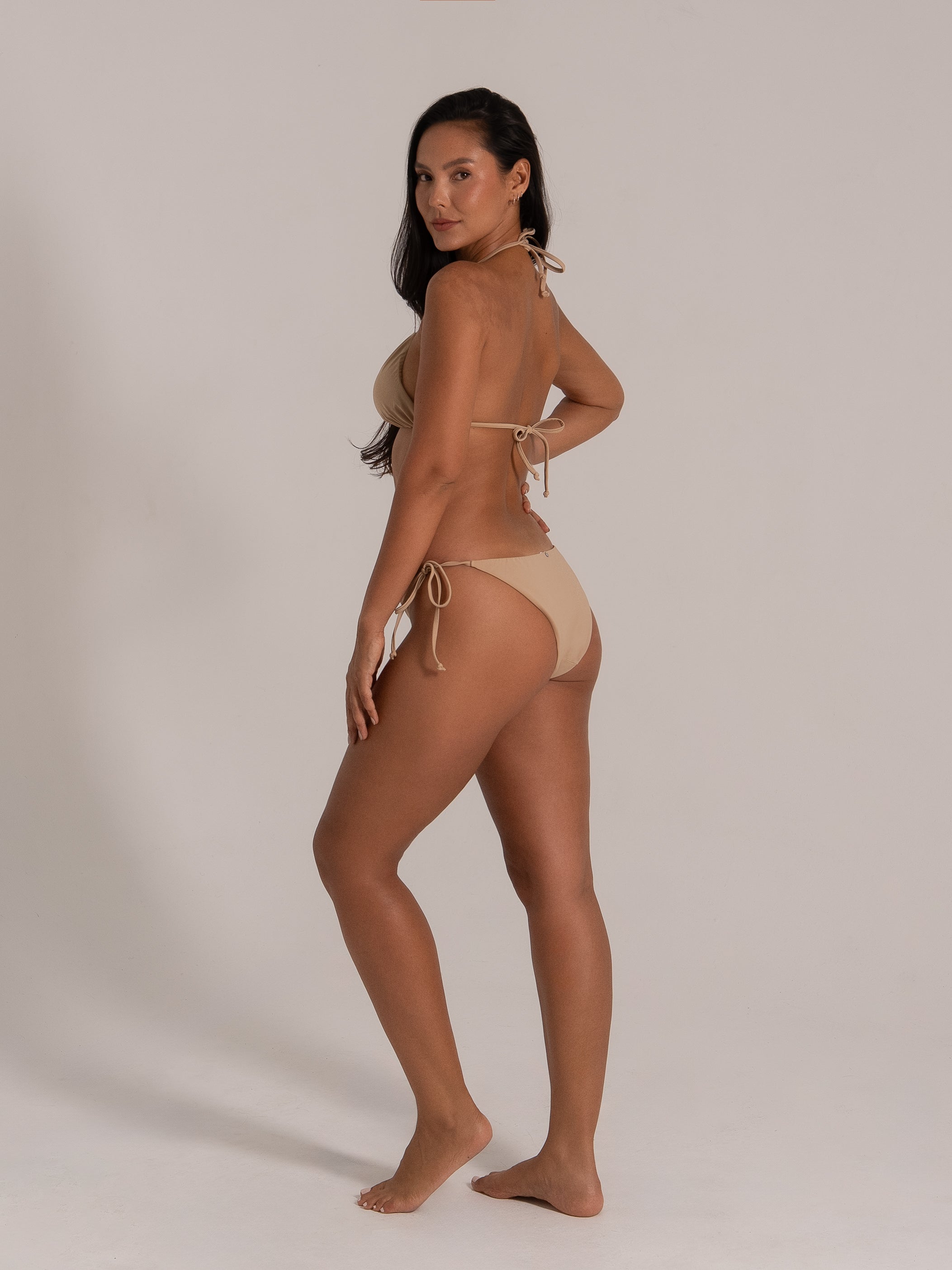Side view of woman in beige halterneck triangle bikini showing minimal coverage and low-rise fit.