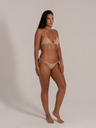 Full frontal view of woman in a nude beige triangle bikini with side tie bottoms.