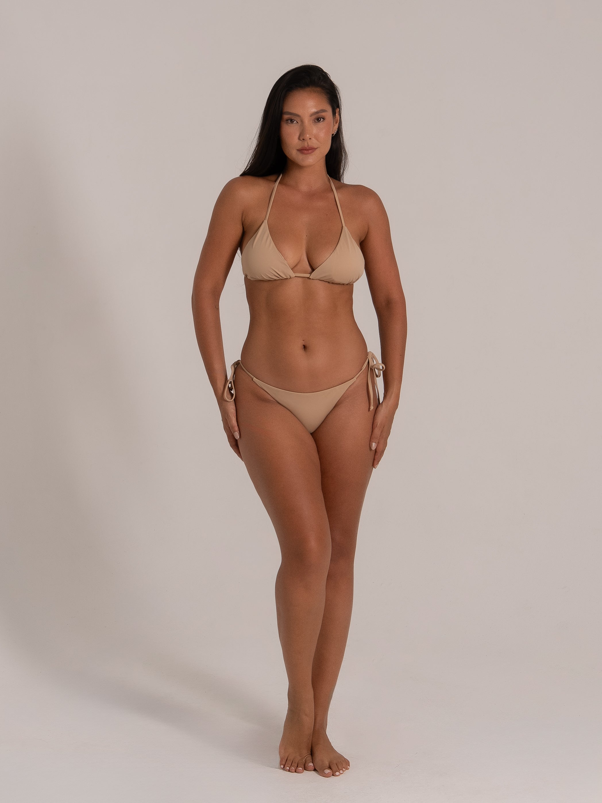 Front close-up view of a woman wearing a beige triangle bikini set with tie sides.