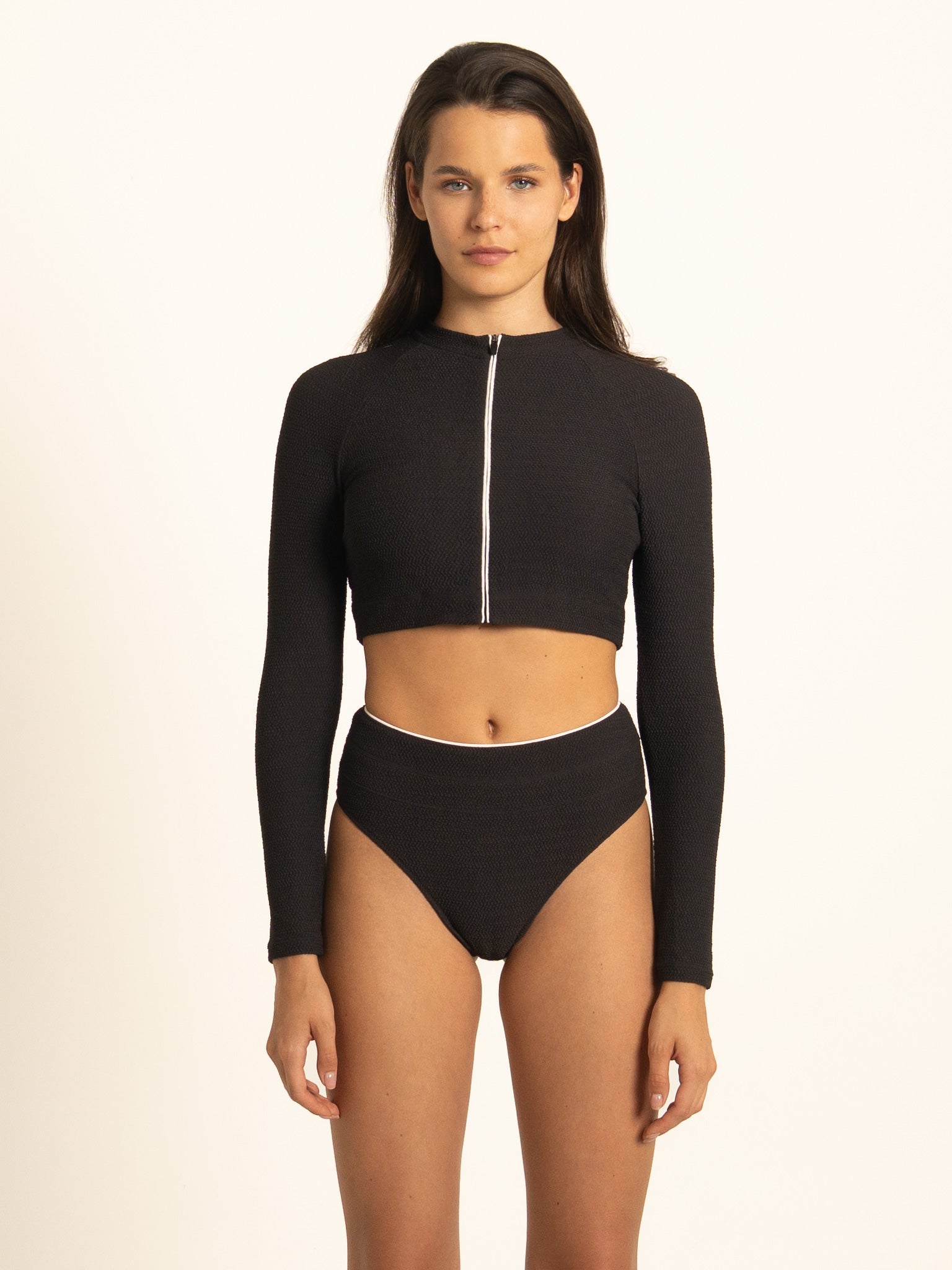 Front view of a woman wearing the Ocean Mystery black long-sleeve rash guard with the front zip fully closed, offering maximum sun protection and a sleek athletic fit.