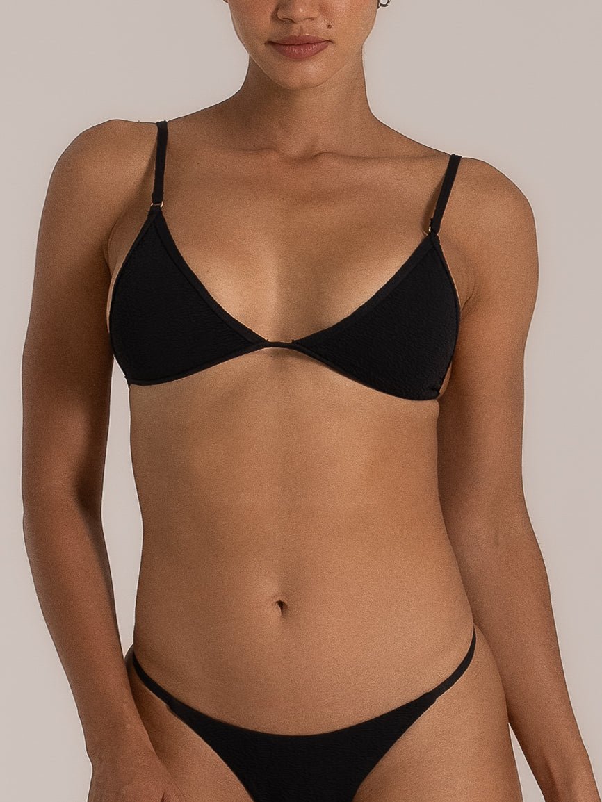Close-up front view of a woman wearing a black textured triangle bikini top with adjustable straps and a matching minimalist bikini bottom.