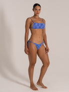 Model posing in a blue camo-textured bikini set with thin shoulder straps and adjustable side ties.
