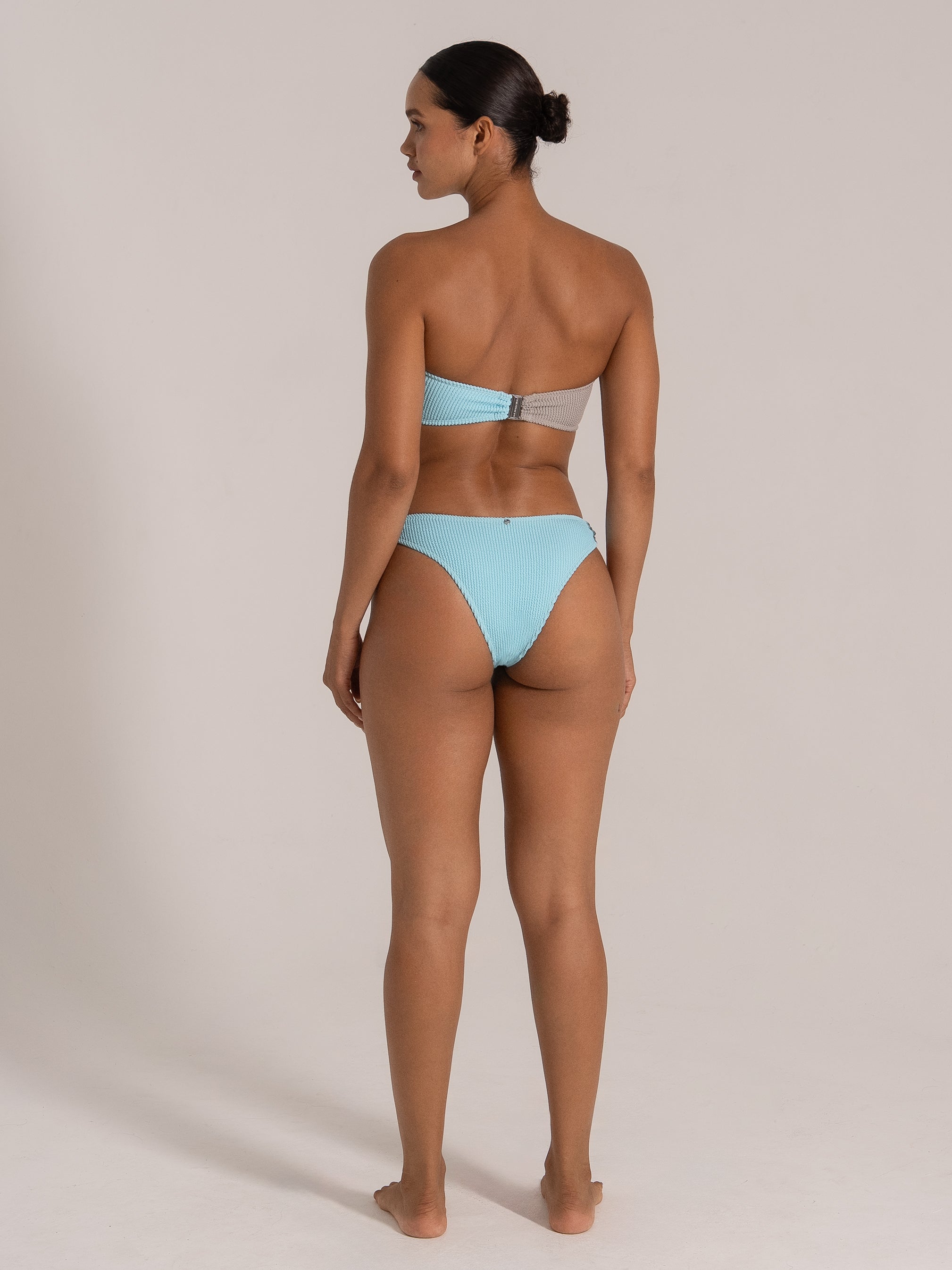 Model wearing blue and grey bandeau bikini set, showing back view with high-cut bottoms.