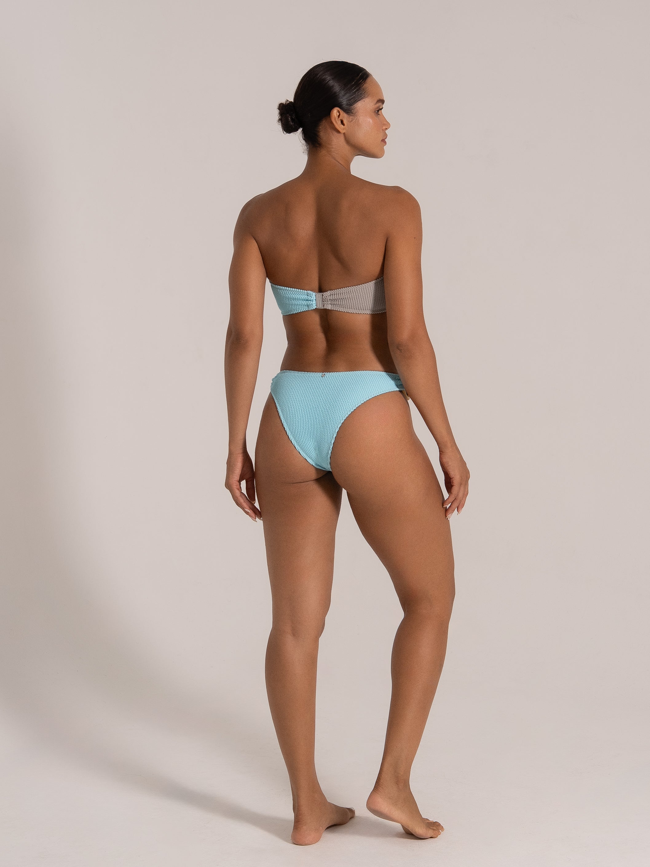 Back-side view of model in two-tone grey and blue bandeau bikini with cheeky cut.