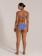Back view of a model wearing a blue textured bikini with adjustable tie sides and spaghetti straps.