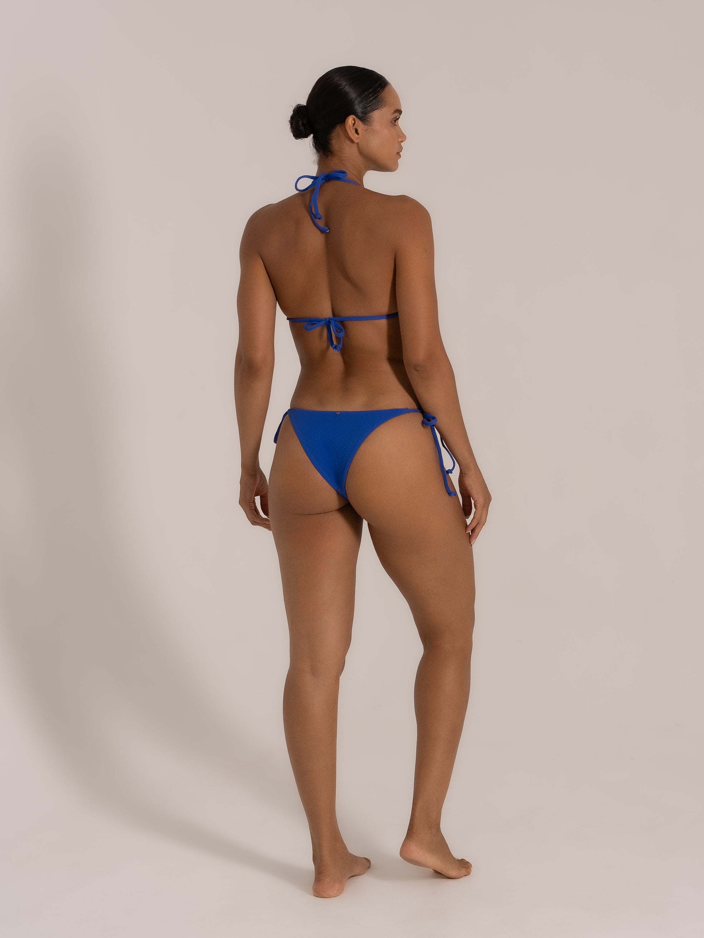 Model wearing blue textured triangle bikini set with halter neck top and tie side bottoms, view 2
