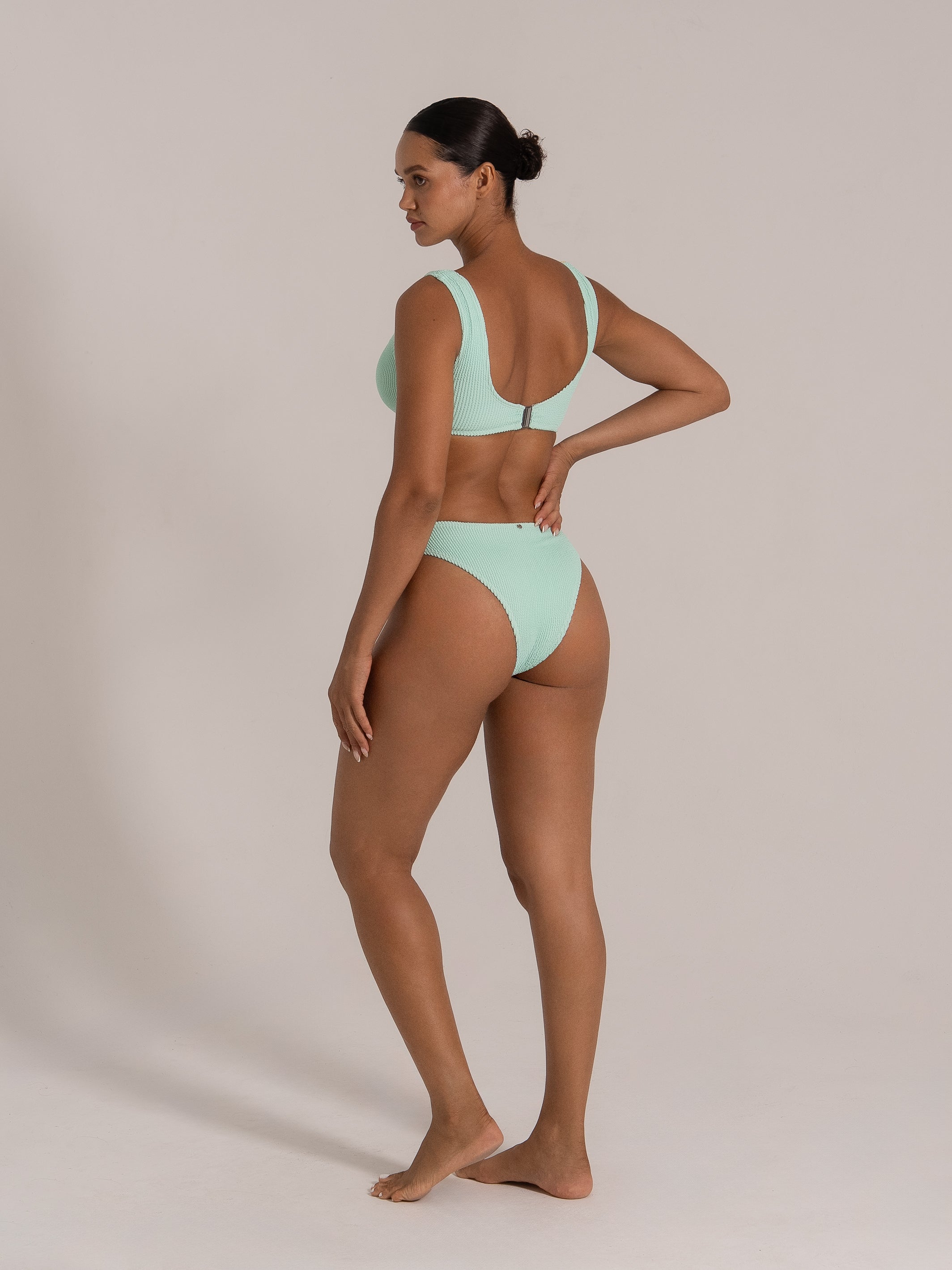 Angled view of a model in a one-shoulder yellow and mint green bikini top with ring accent and coordinating high-waisted mint bottom.