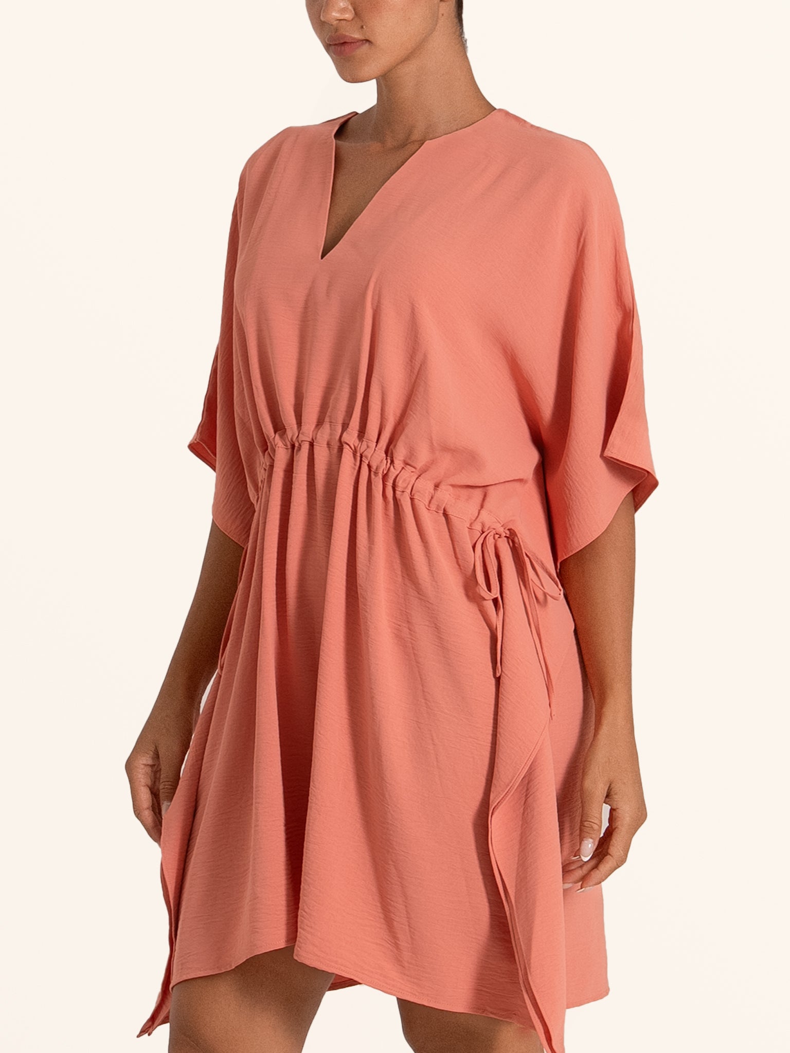 Side profile of coral pink mini dress with short wide sleeves and cinched waist