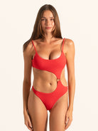 Front view of woman wearing red textured cut out one piece swimsuit with scoop neckline and waist ring detail.