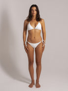 Front view of woman wearing white triangle bikini top and tie-side bikini bottoms