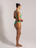 Side angle of a model in a green bikini set with scoop neckline and mid-rise cheeky bottoms, posing confidently in studio light.