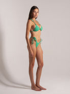 Side view of woman wearing green textured halter bikini with triangle top and tie-side bottoms