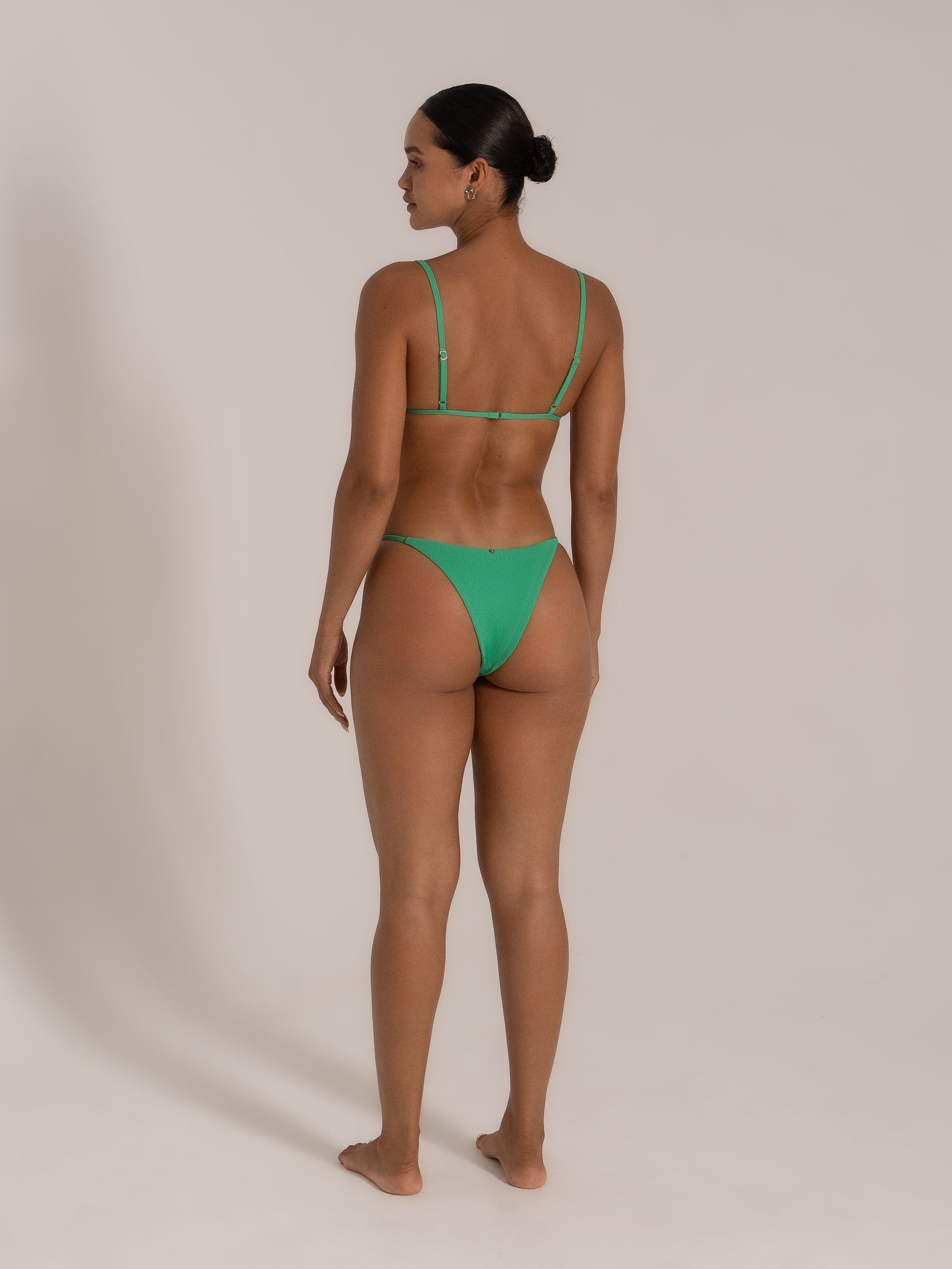 Back view of model in green textured triangle bikini with adjustable straps