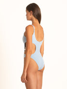 Side view of woman wearing light blue one-piece swimsuit with side cutout and scoop back