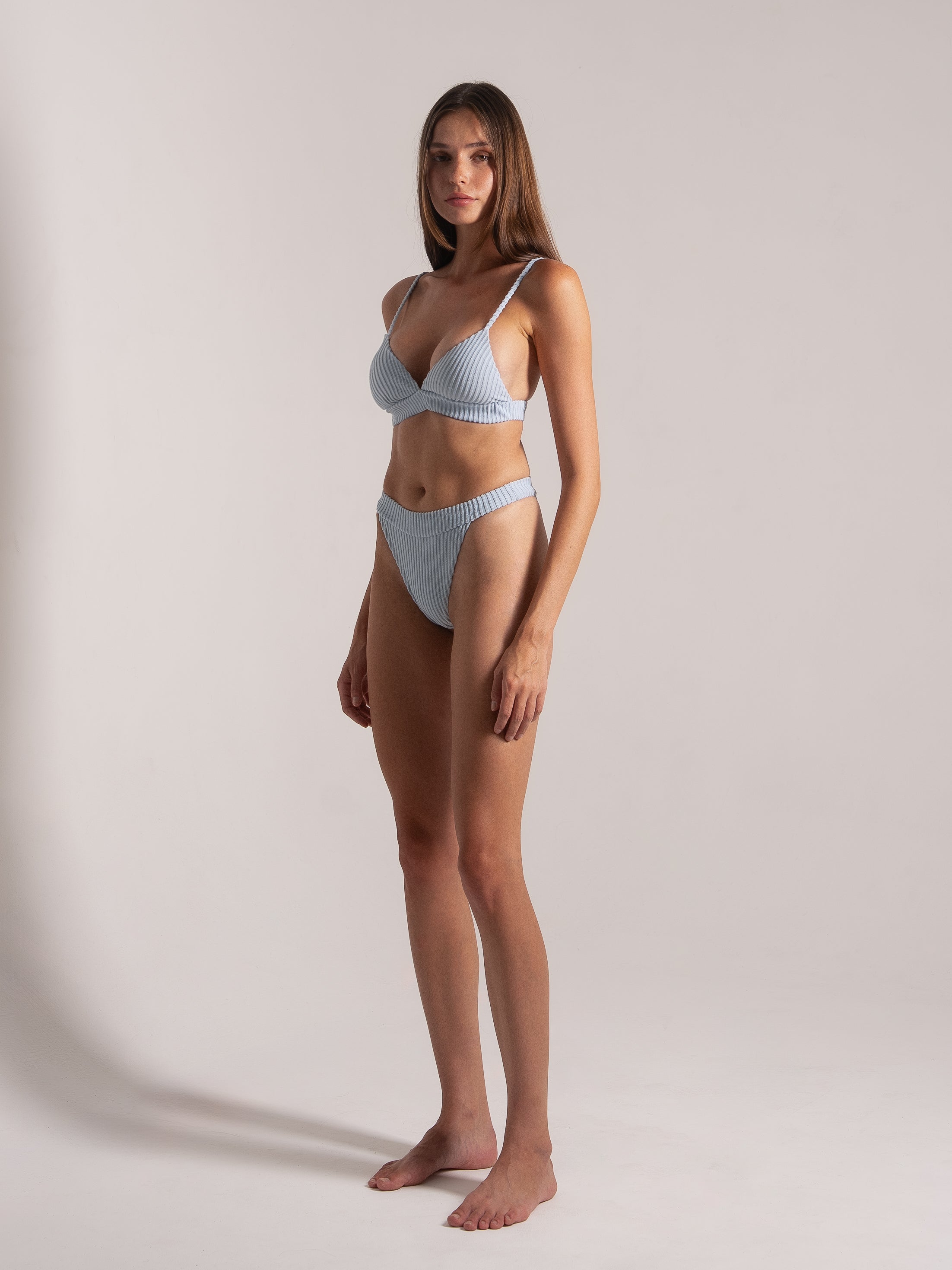 Woman in light blue ribbed bikini set with high-cut bottoms, shown from an angled side view