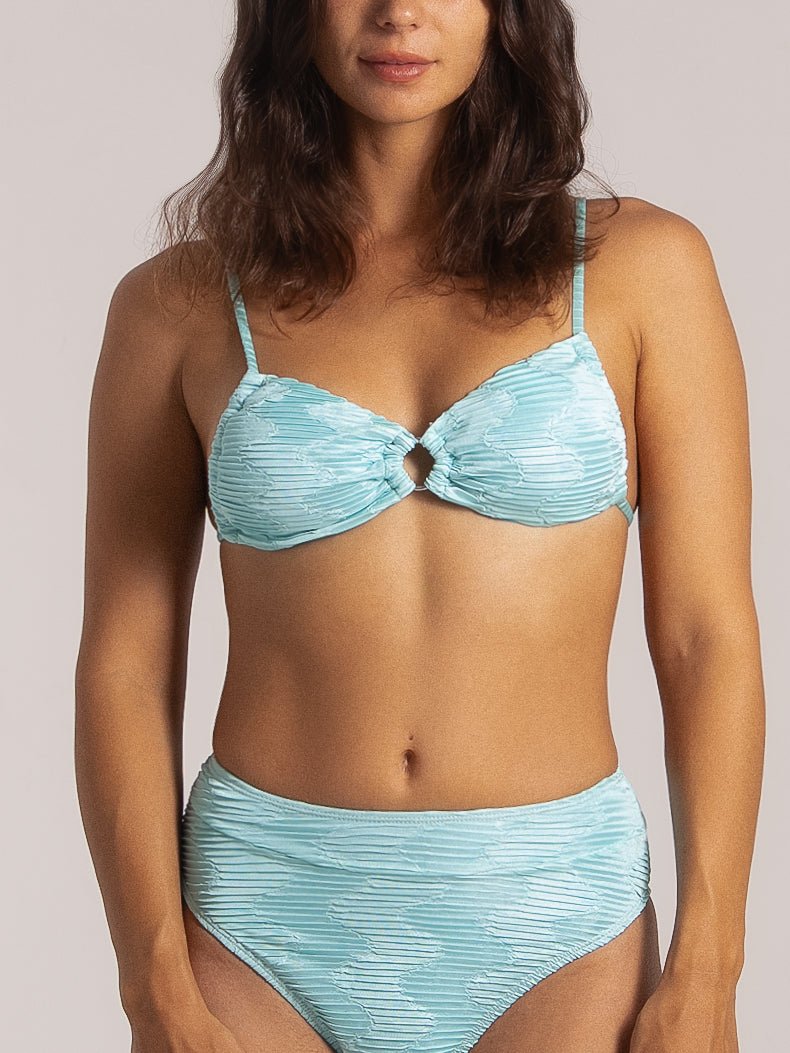 Front view of a woman wearing a light blue ruched bikini with a front ring detail and high-waisted bottoms, designed for a flattering and retro-inspired beach look.