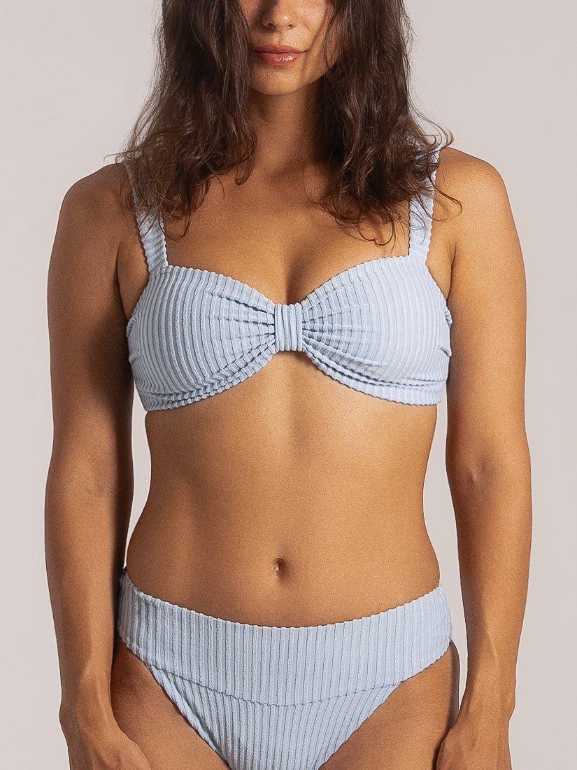 Model wearing a light blue textured bikini set featuring a knotted bandeau top and wide waistband high-cut bottoms.