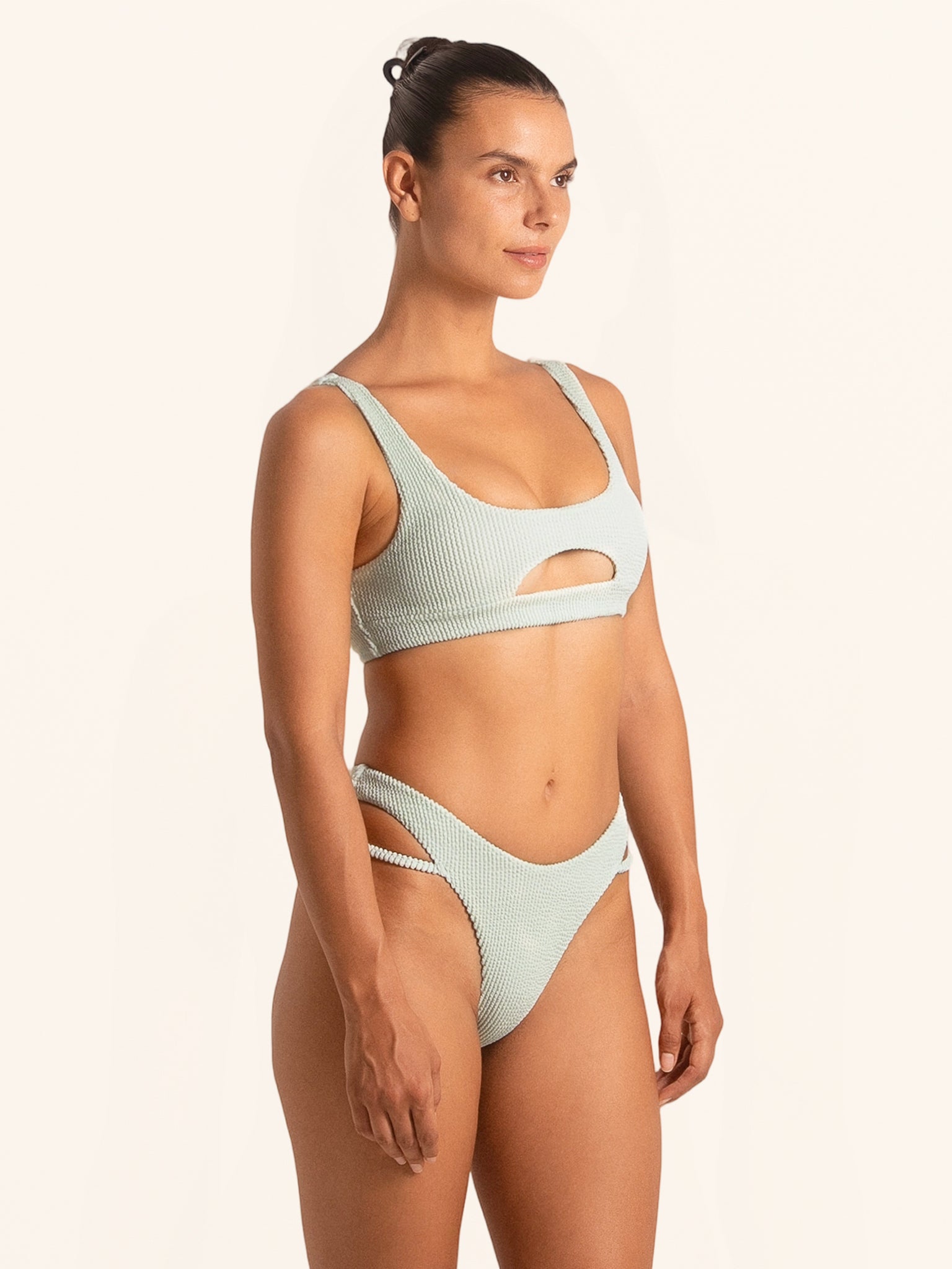 Three-quarter view highlighting waist cut-out design on light green bikini bottom.