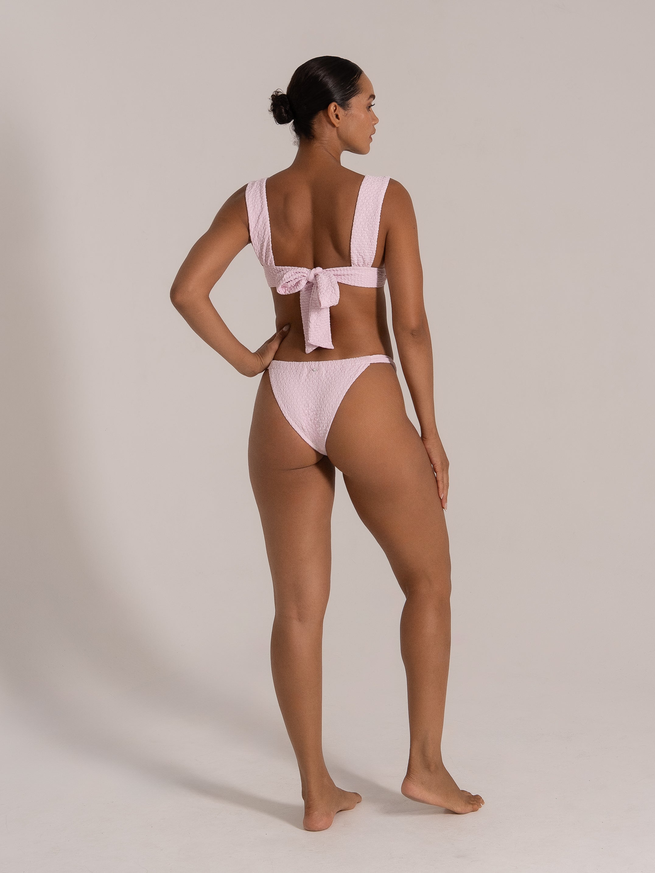 Side angle of a light pink bikini set featuring thick shoulder straps and a statement bow back.