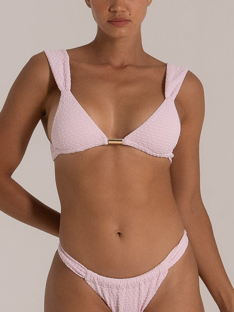 Close-up front view of a light pink textured bikini set featuring wide shoulder straps and a gold metal bar at the center.
