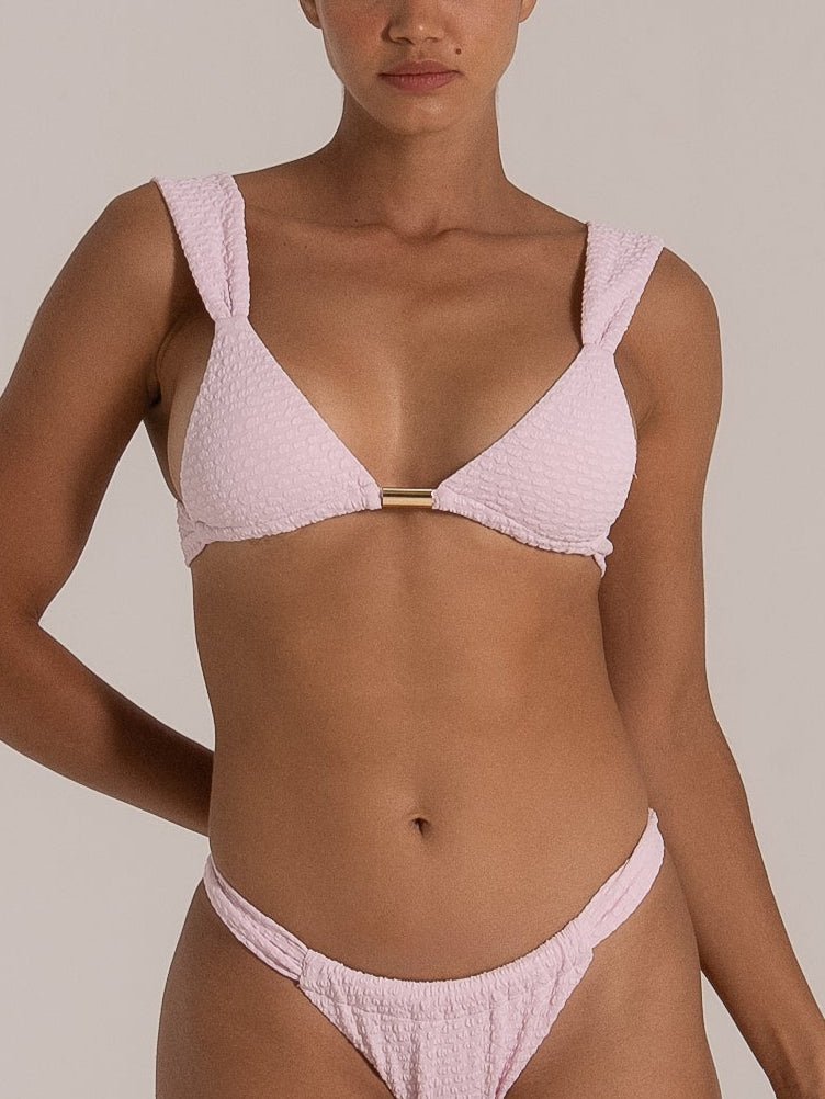 Close-up front view of a light pink textured bikini set featuring wide shoulder straps and a gold metal bar at the center.