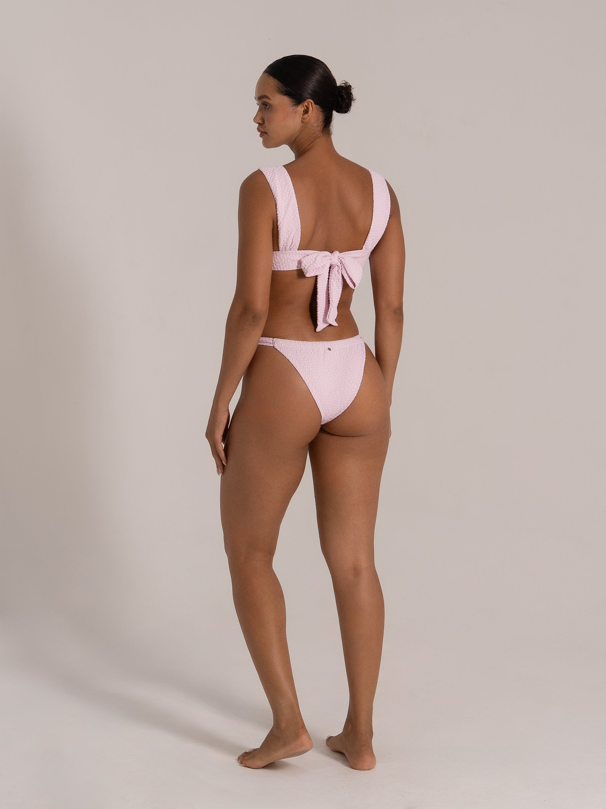 Back view of a light pink textured bikini set with wide straps and a large bow tie closure.