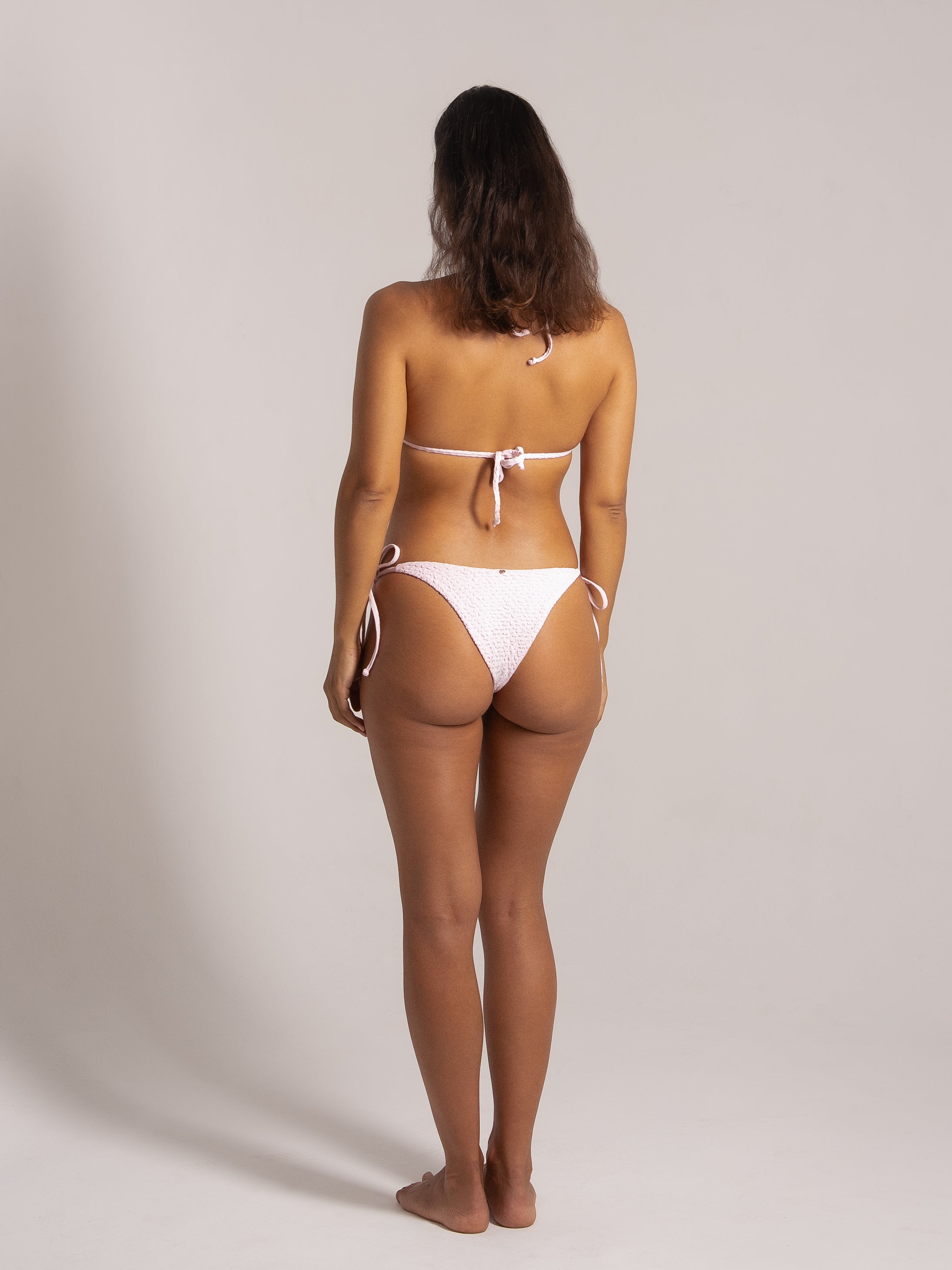 Back angled view of a light pink crinkle bikini with halter top and adjustable tie back.