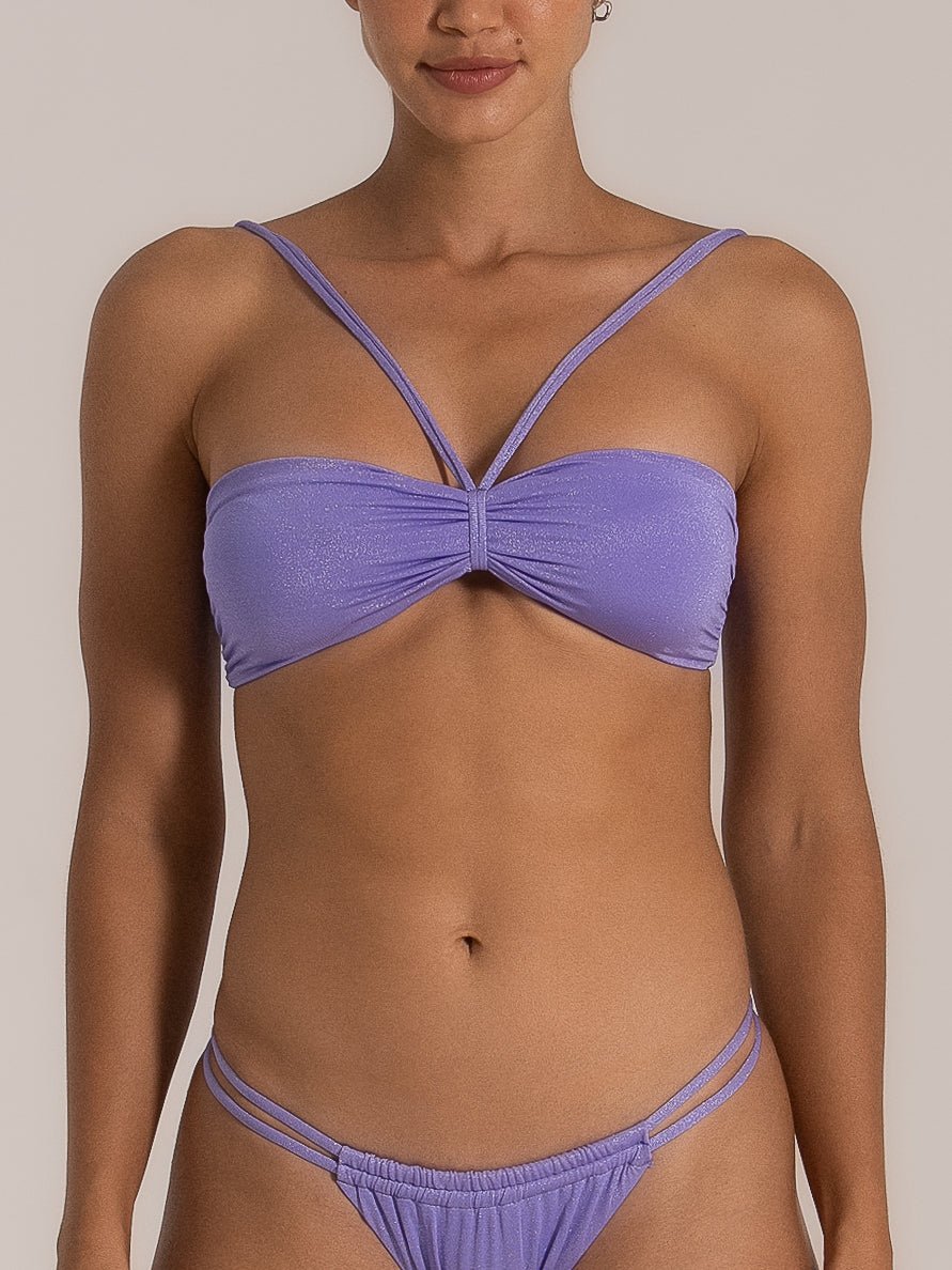Front view of a woman wearing a lilac bandeau bikini set featuring criss-cross straps on the top and double side straps on the bottoms, styled in a shimmering fabric for a standout beach look.