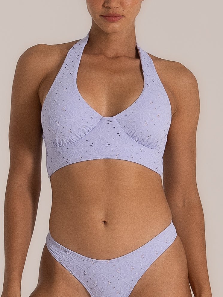 Front view of a woman wearing a lilac halter bikini set featuring delicate floral embroidery, eyelet cutout details, a plunging neckline, and matching low-rise bottoms.