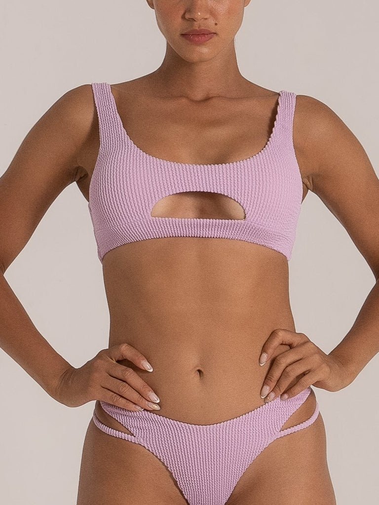Model wearing lilac textured bikini set with scoop neck and front cutout detail, paired with double-strap high-leg bikini bottoms.