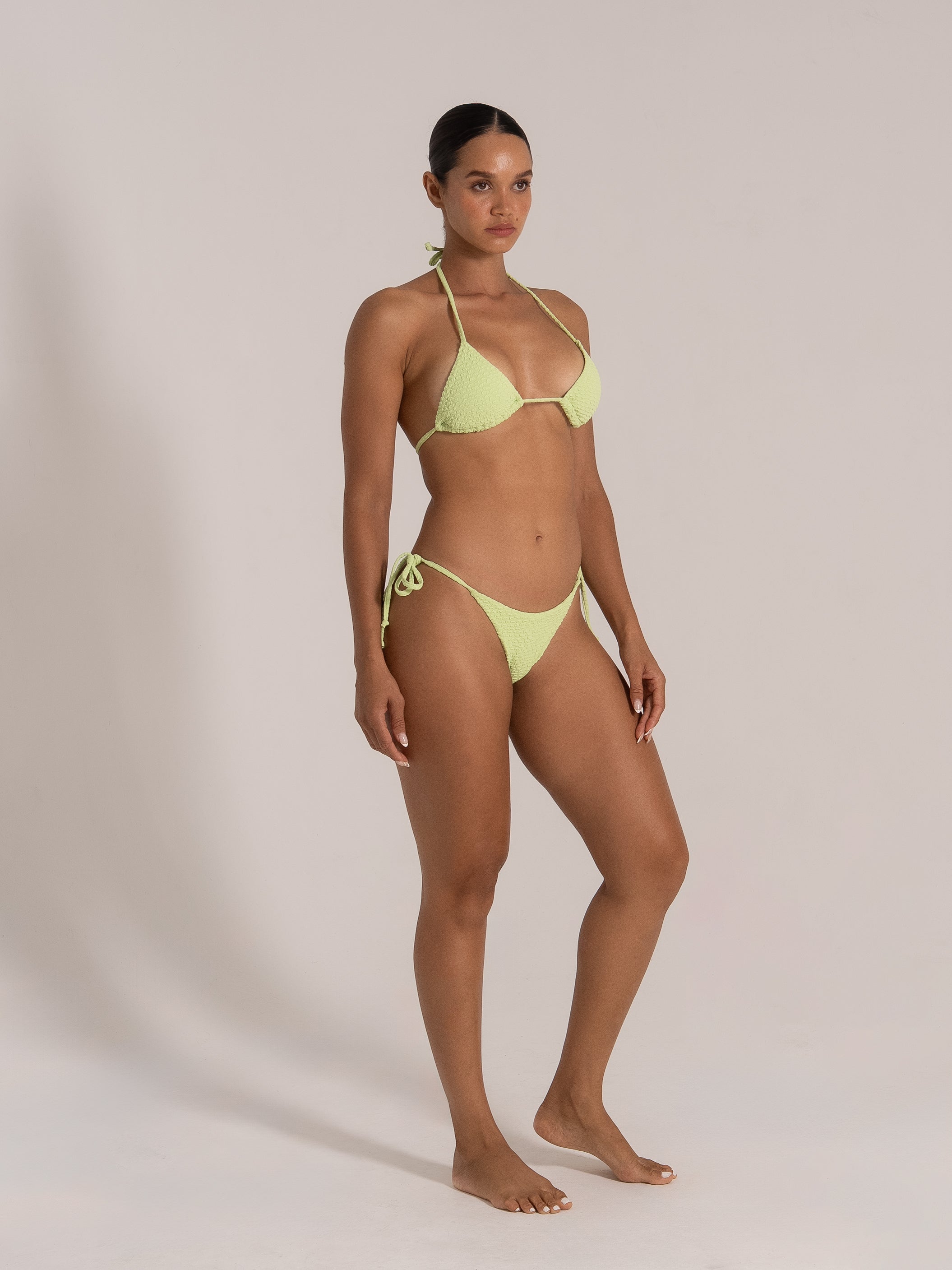 Model posing in a textured lime green bikini set, showcasing side angle with adjustable tie sides.