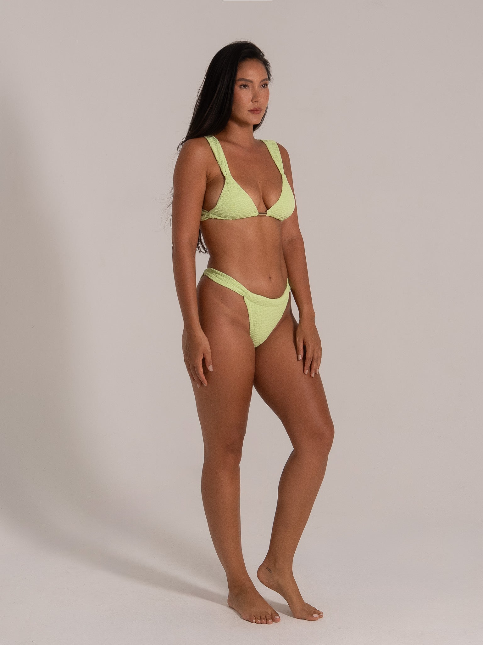 Woman in lime green bikini with thick straps and triangle top, high-waisted bottoms, side angle