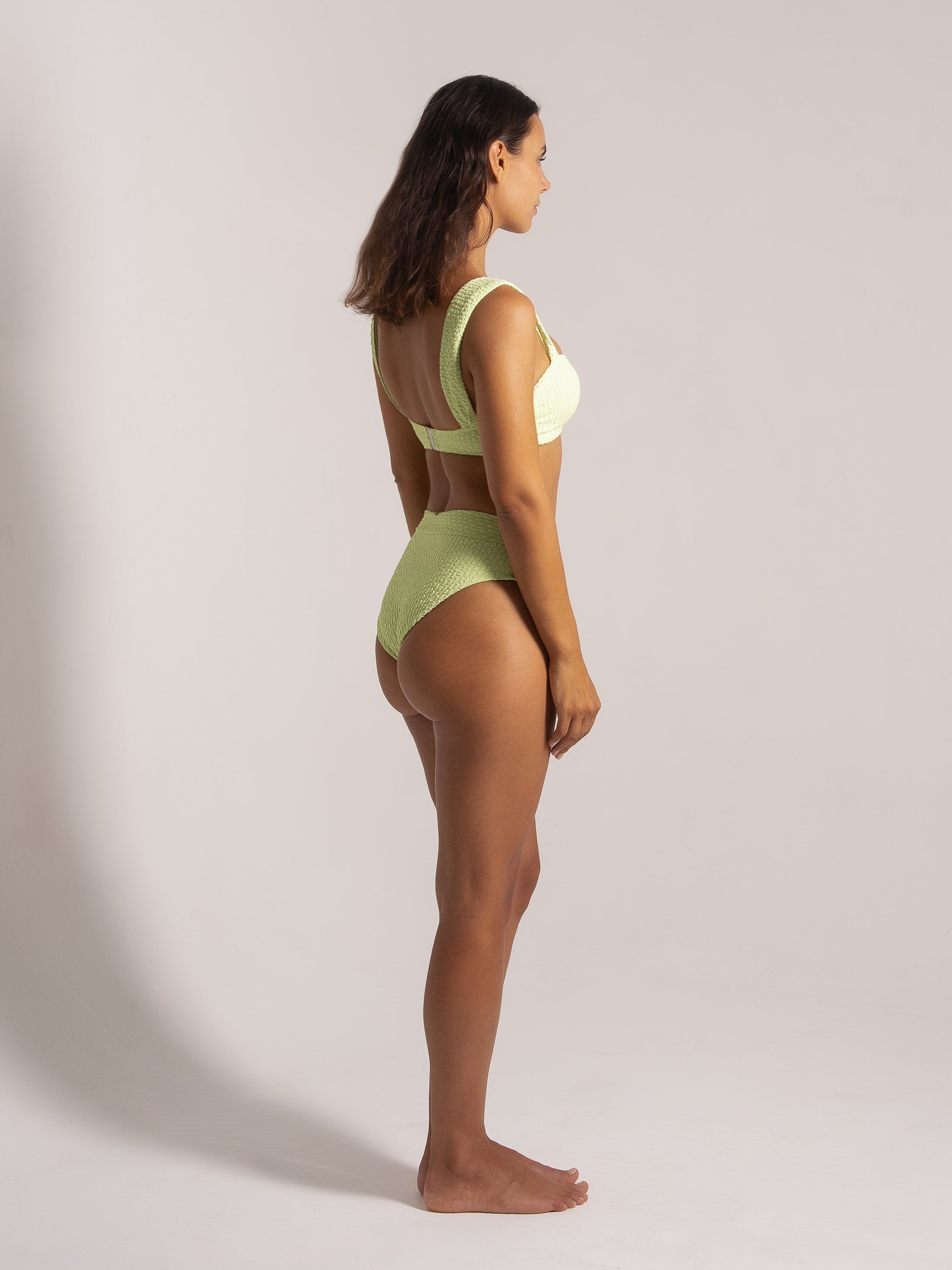 Model in lime bikini set posing at three-quarter angle, showing textured fabric and flattering fit