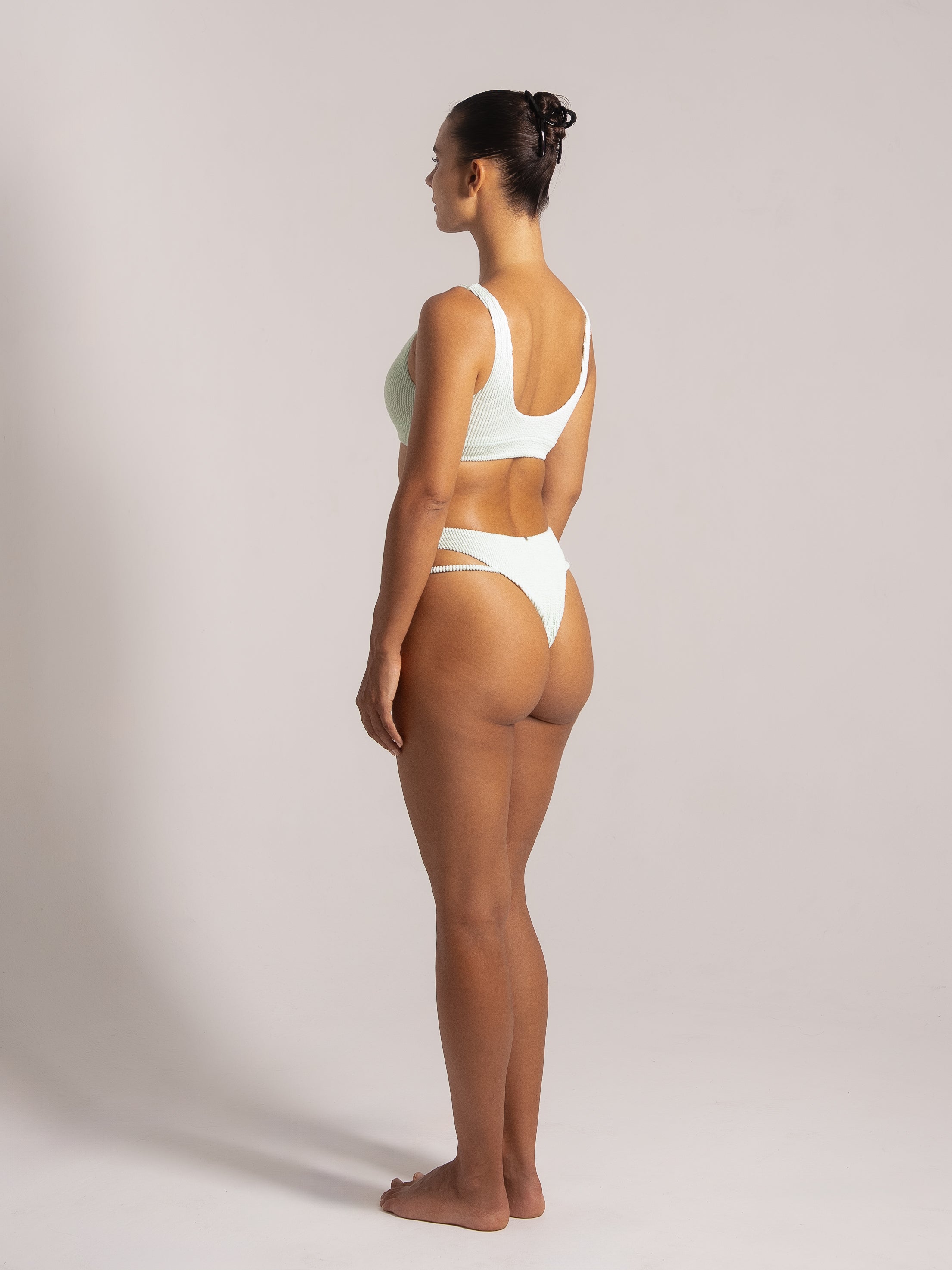 Woman in mint green textured bikini with scoop back top and high-cut double-strap bottoms, back side angle view
