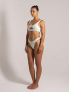 Woman in mint green textured bikini with front cut-out top and high-cut double-strap bottoms, side view