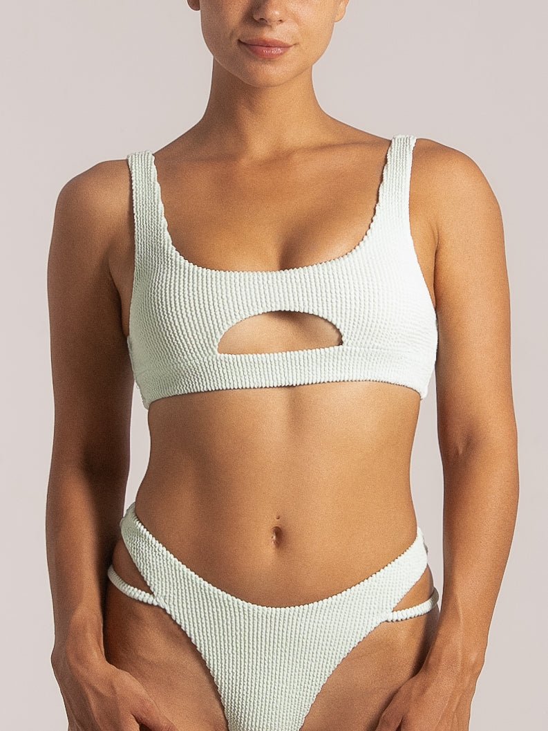 Front close-up of a woman wearing a mint green textured bikini with a front cutout top and side-strap high-waisted bottoms, showcasing a bold and modern design.