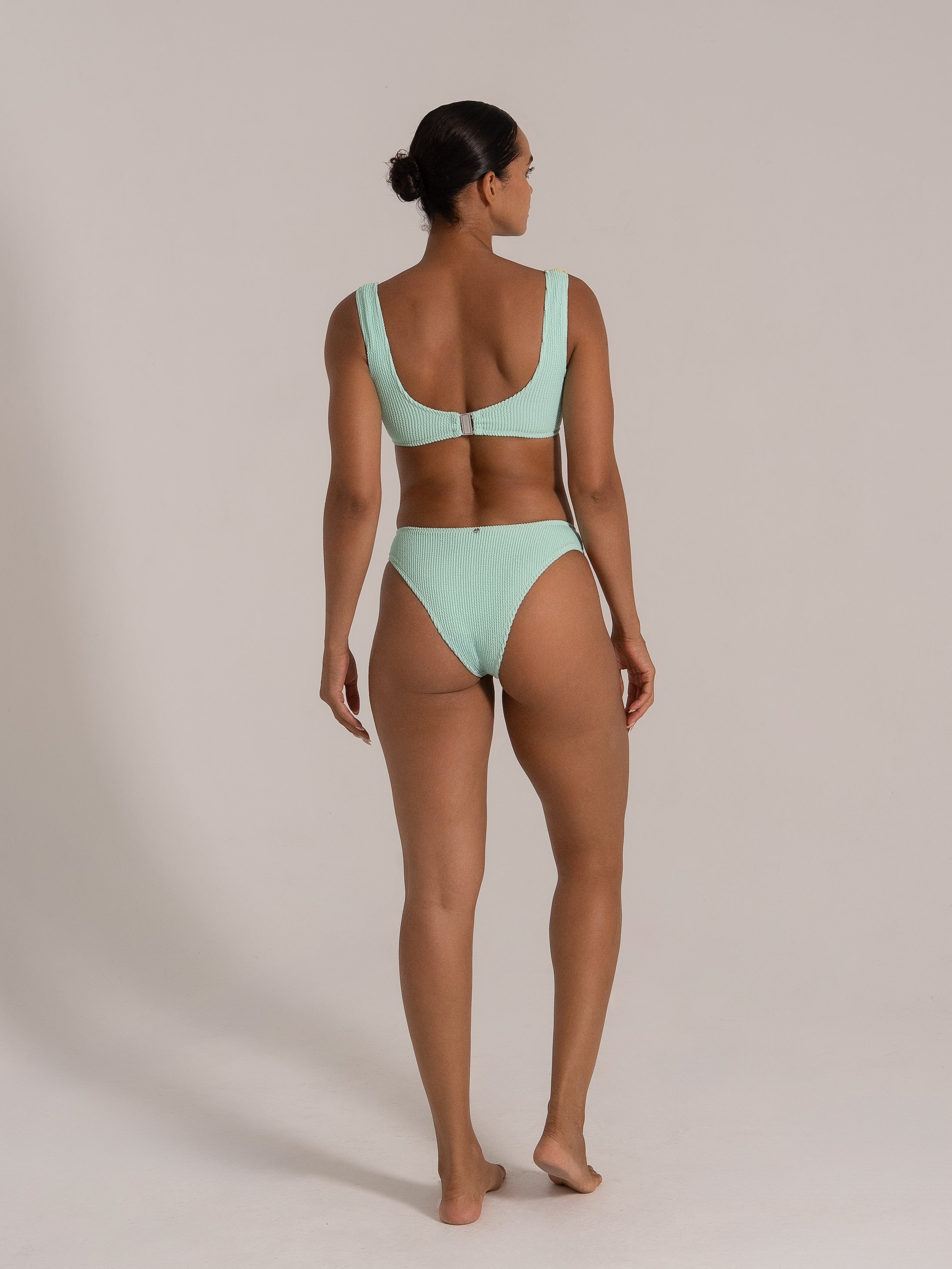Back view of a model wearing a mint green textured bikini set with a clasp closure and high-waisted bottom.