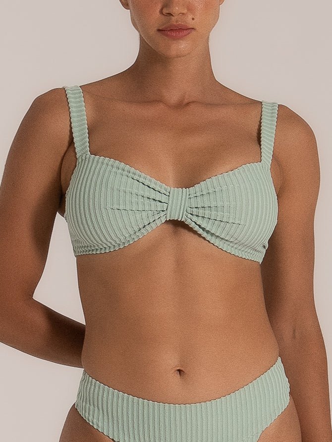 Close-up front view of a woman wearing a mint green ribbed bikini set, featuring a sweetheart neckline with a central bow detail and wide shoulder straps, paired with a high-leg matching bottom.