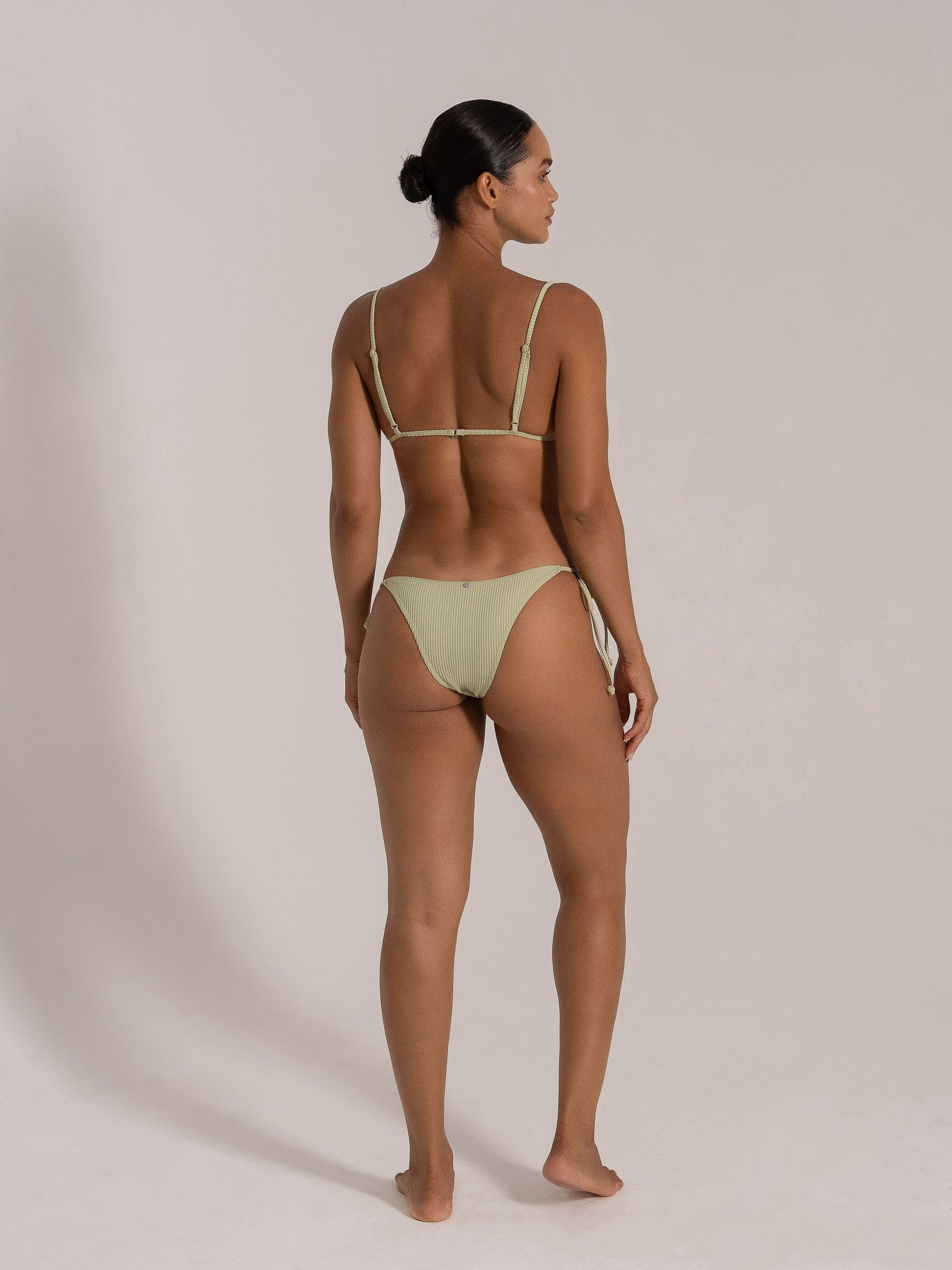 Side-back view of a woman in mint green ribbed triangle bikini with adjustable straps and tie side bottom