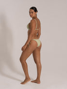 Woman in light green ribbed bikini looking over shoulder, side view of tie side swimwear set