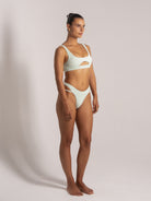 Woman wearing a mint green textured bikini featuring a front cut-out top and high-leg cut-out bottoms