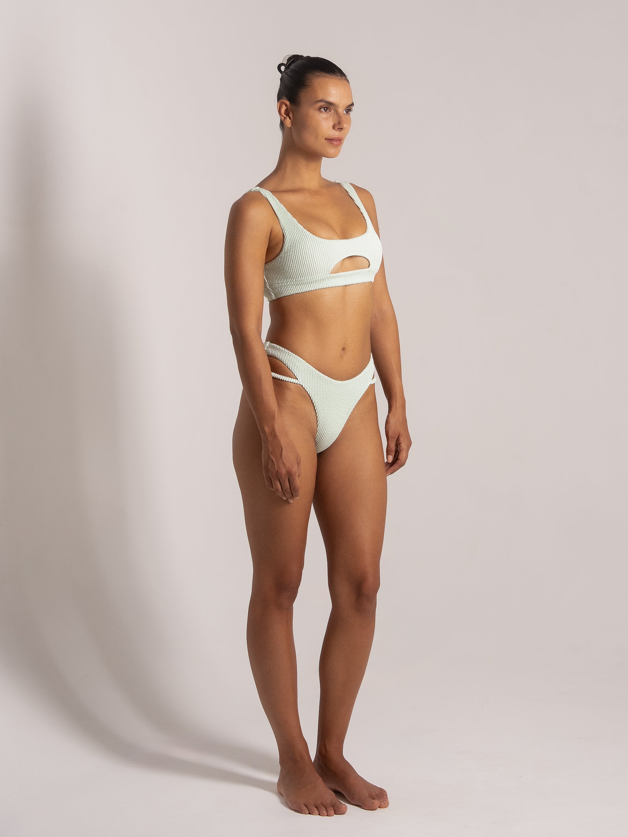 Woman wearing a mint green textured bikini featuring a front cut-out top and high-leg cut-out bottoms