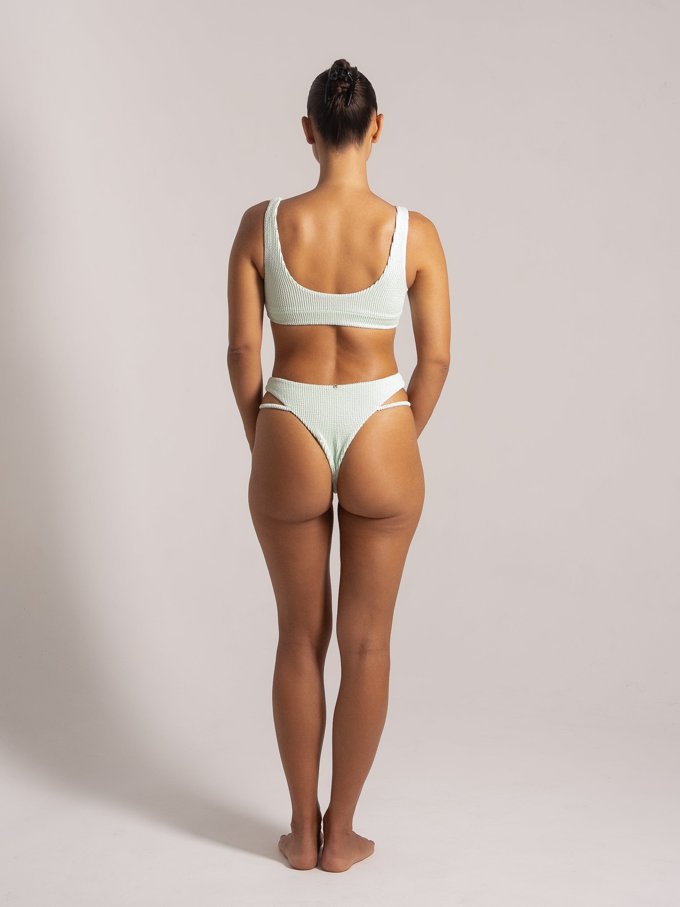 Back view of a woman wearing a mint green textured high-waisted bikini with thick shoulder straps and cut-out side details on the bottom