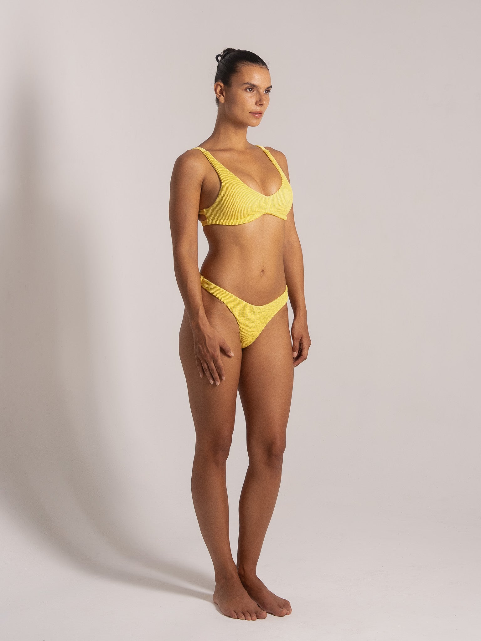 Model wearing yellow textured bikini set featuring scoop neckline and wide straps