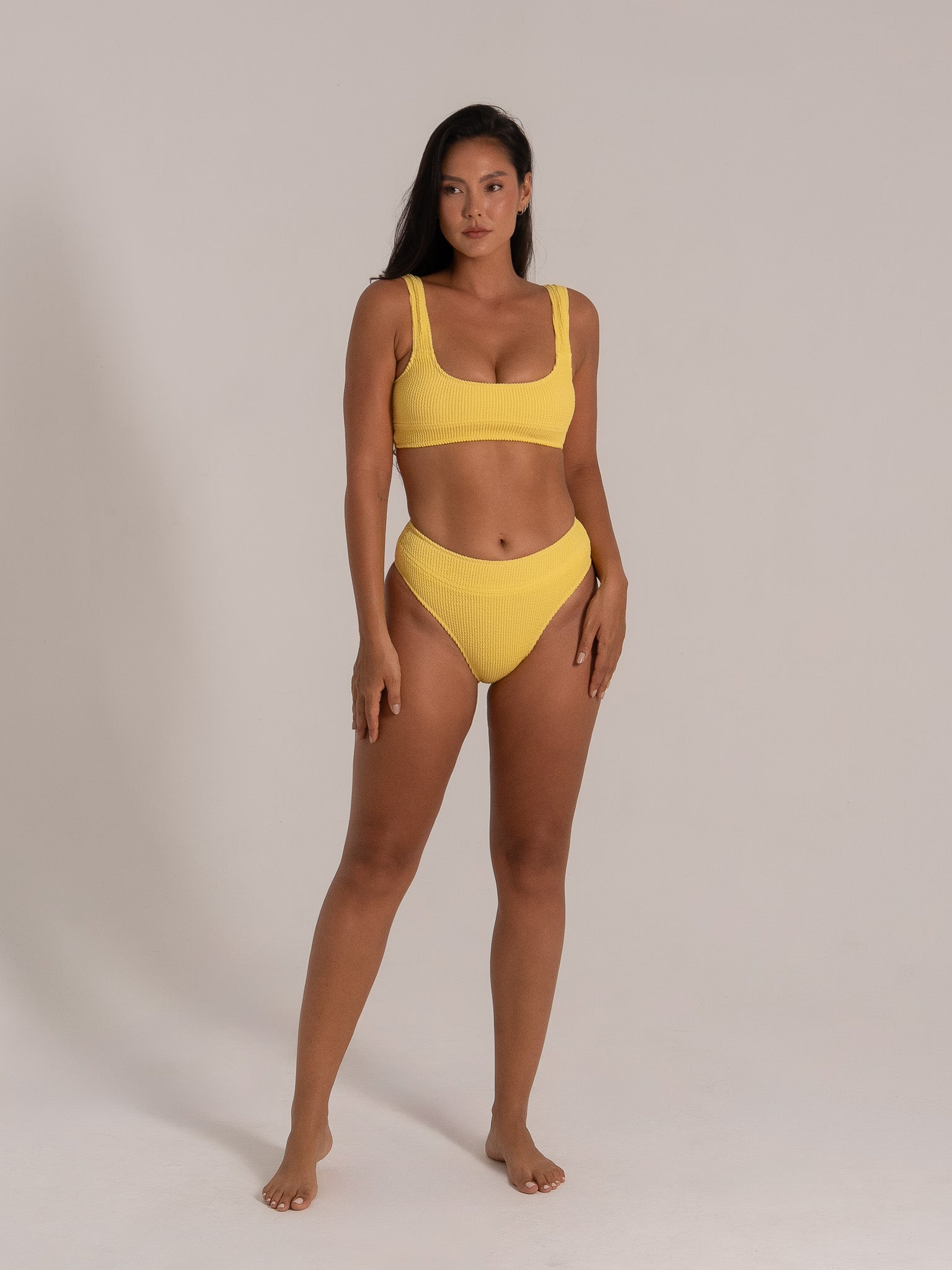 Woman posing in front view wearing mustard yellow textured bikini set with square neckline and thick straps