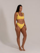 Model in mustard yellow ribbed bikini set with high-waisted bottoms and wide shoulder straps in front angle