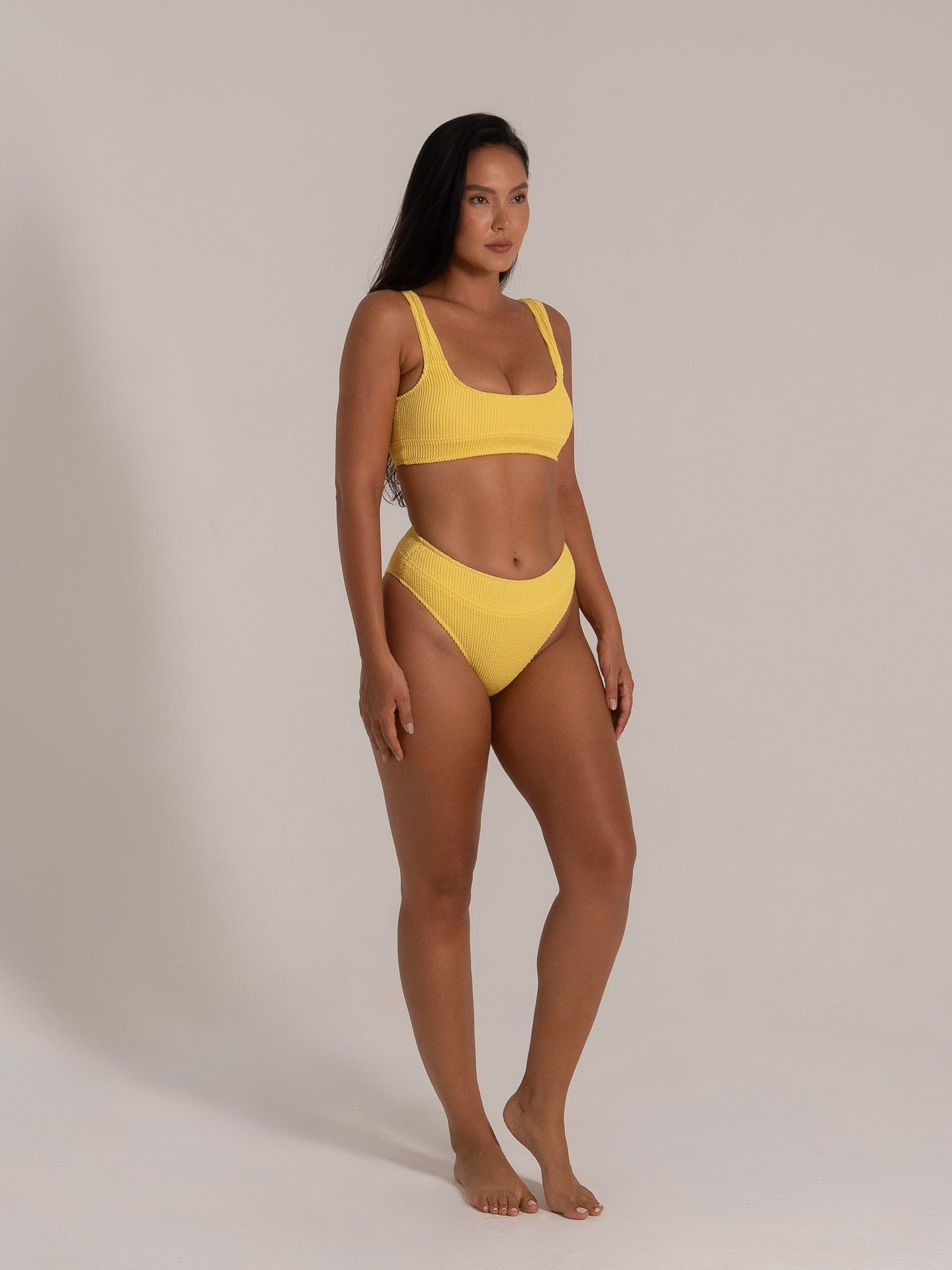 Model in mustard yellow ribbed bikini set with high-waisted bottoms and wide shoulder straps in front angle