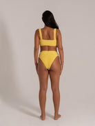 Back view of woman wearing mustard yellow textured bikini set with thick shoulder straps and high-waisted bottoms